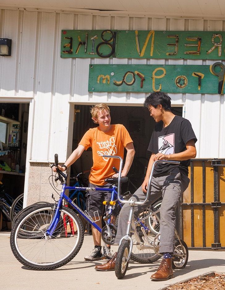 Students talk while sitting on bikes outside the Green Bike Program shed